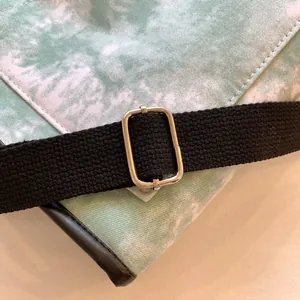Detail of silver metal buckle and black canvas strap on tie-dye shoulder bag