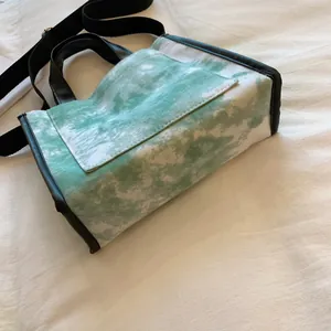 Detail view of tie-dye green canvas tote bag with black leather trim and shoulder strap