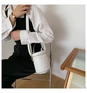 Nahaufnahme einer weißen zylindrischen Beuteltasche mit Krokoprägung und Goldlogo