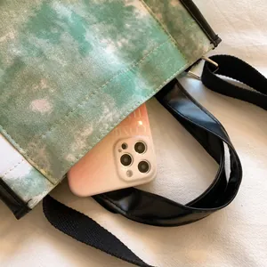Detail of green tie-dye canvas tote bag featuring black leather trim and wide shoulder strap