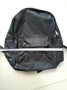 Detailweergave van zwarte nylon rugzak op vloer met meetlint die de breedte van 32 cm toont