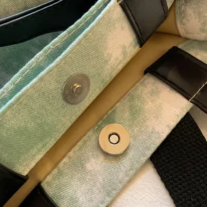 Detail of silver magnetic buckle and leather stitched handles on a green canvas tote