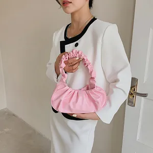 Vista detallada del bolso plisado rosa con asa fruncida sobre una modelo con blazer