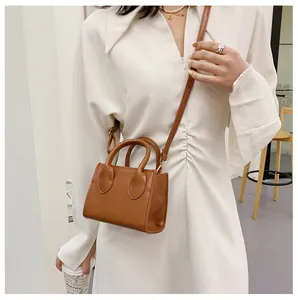 Brown mini square bag with dual handles and adjustable strap styled on a white dress