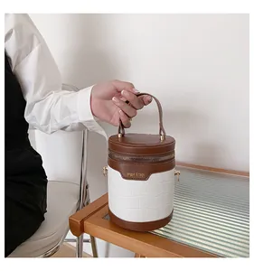 Detail einer braun-weißen Zylinder-Beuteltasche mit goldenem Reißverschluss auf Holztisch