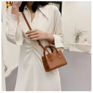 Detail of a brown leather crossbody bag styled with a white dress for daily leisure