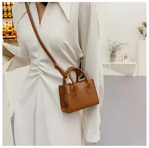 Detailed view of mini brown crossbody bag worn with a white dress in a lifestyle setting