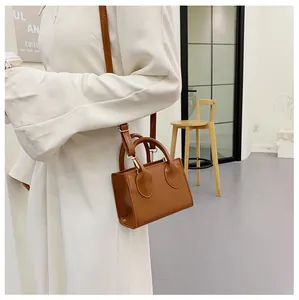 Close-up of a brown mini square leather bag worn cross-body with adjustable strap
