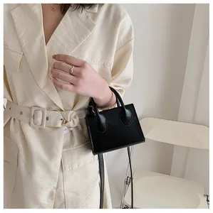 Chic black mini square handbag with dual handles worn by model in a stylish trench coat