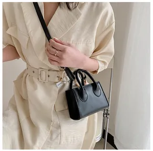 Close-up of black mini tote bag with dual handles and crossbody strap on a model