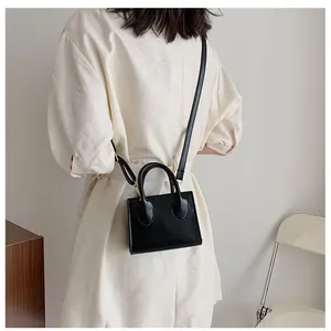 Minimalist black mini square bag with gold ring handles and thin shoulder strap details