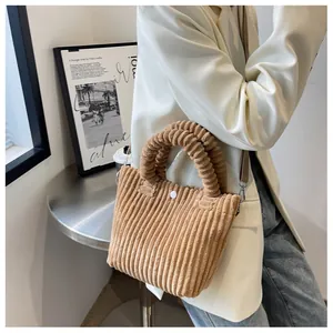 Detail of brown corduroy bucket bag featuring a unique wavy handle and magnetic snap closure