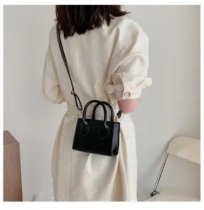 Detail of a mini black PU leather crossbody bag with gold hardware on a female model