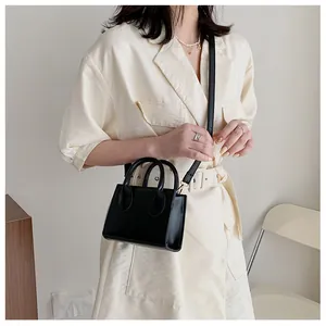 Close-up of a small black PU leather crossbody bag with dual handles and long strap