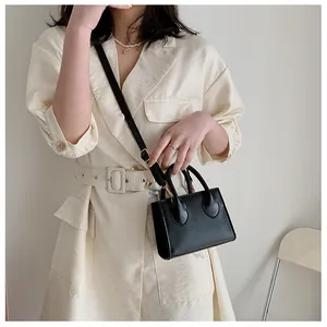 Close-up of a minimalist black square crossbody bag with gold hardware and leather texture