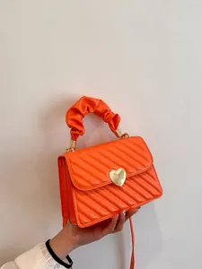 Close-up of orange quilted crossbody bag featuring a golden heart metal clasp and ruched handle