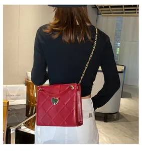 Sac bandoulière rouge matelassé avec fermoir cœur doré et chaîne porté par un mannequin