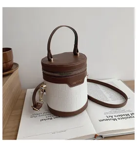 Details einer zylindrischen Eimertasche in Braun und Weiß mit Krokodilprägung und Goldreißverschluss
