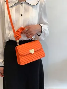 Detail of bright orange quilted crossbody bag with heart-shaped gold clasp and ruched handle