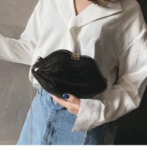 Detail of black glossy lip-shaped crossbody bag with gold chain strap on a model