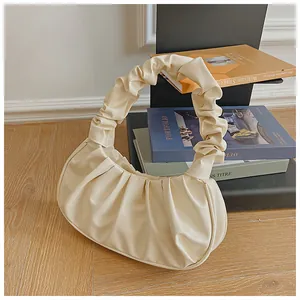 Detalle del bolso nube plisado blanco crema con asa estilo scrunchie sobre libros