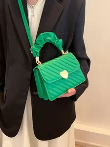 Detail of green quilted crossbody bag with heart buckle and pleated handle on black blazer