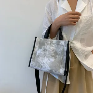 Detailed shot of a marble pattern canvas tote bag with black strap held by a model