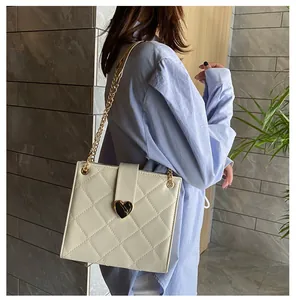 Sac à bandoulière matelassé blanc avec fermoir cœur doré et chaîne, porté par un mannequin