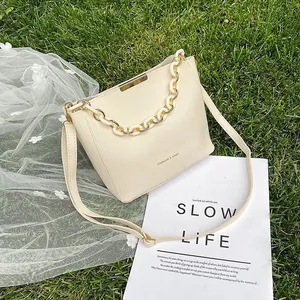 Creamy bucket bag with chain handle and adjustable strap on a natural lawn background