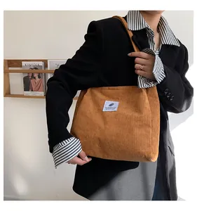 Close-up of brown corduroy tote bag with white square logo patch on stylish female model