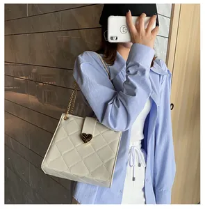 Détail du sac bandoulière matelassé blanc avec fermoir coeur doré porté par le mannequin