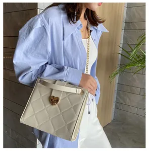 Modèle portant un sac bandoulière matelassé crème avec une boucle cœur en métal doré