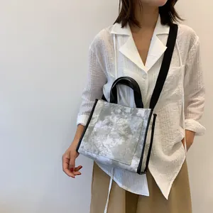 Detail of gray tie-dye canvas tote bag with black leather trim and wide shoulder strap
