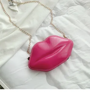 Detail of high-gloss pink lip-shaped crossbody bag with gold chain strap on white fabric
