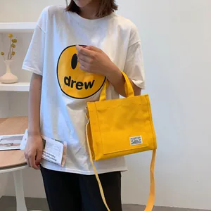 Detail view of yellow canvas tote bag with white woven label and adjustable shoulder strap