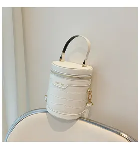 Detail der weißen Zylindertasche mit Krokodilprägung und goldenen Beschlägen