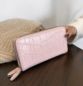Pink faux leather long wallet with crocodile texture held in hand against wooden desk