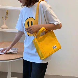 Detail view of yellow canvas tote bag with adjustable shoulder strap and woven label on a model