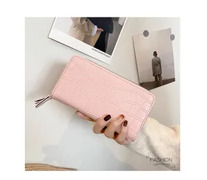 Pink long crocodile texture wallet with wrap-around zipper detail held by hand