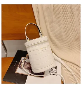 Detailaufnahme einer weißen Zylindertasche mit Kroko-Prägung auf einem Holzstuhl mit Magazin