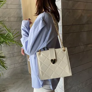 Sac à bandoulière matelassé blanc avec fermoir cœur doré et chaîne porté par mannequin