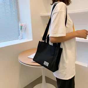 Side view of a minimalist black canvas tote bag worn on shoulder in a bright room