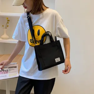 Detail of black canvas tote bag with adjustable shoulder strap and white woven brand label