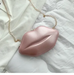 Macro view of a soft pink lip-shaped crossbody bag with a glossy finish and gold chain