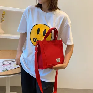 Detailed view of red canvas tote bag with woven label and adjustable crossbody strap