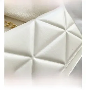 Macro shot of white crossbody bag featuring geometric triangle embossed texture and gold chain