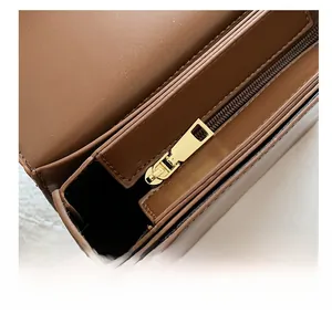 Close-up of smooth gold metal zipper and stitching detail on a brown leather shoulder bag