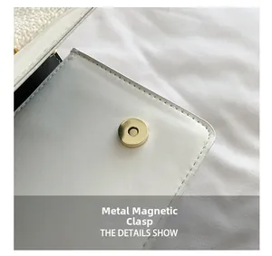 Close-up of golden magnetic hardware closure on white leather and plush small square bag