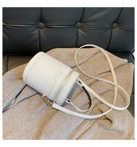 Detailansicht der weißen Zylindertasche mit Krokodilmuster, Goldbeschlägen und schwarzen Akzenten