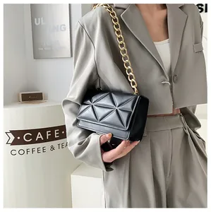 Detail of black geometric quilted crossbody bag with chunky gold chain strap on model